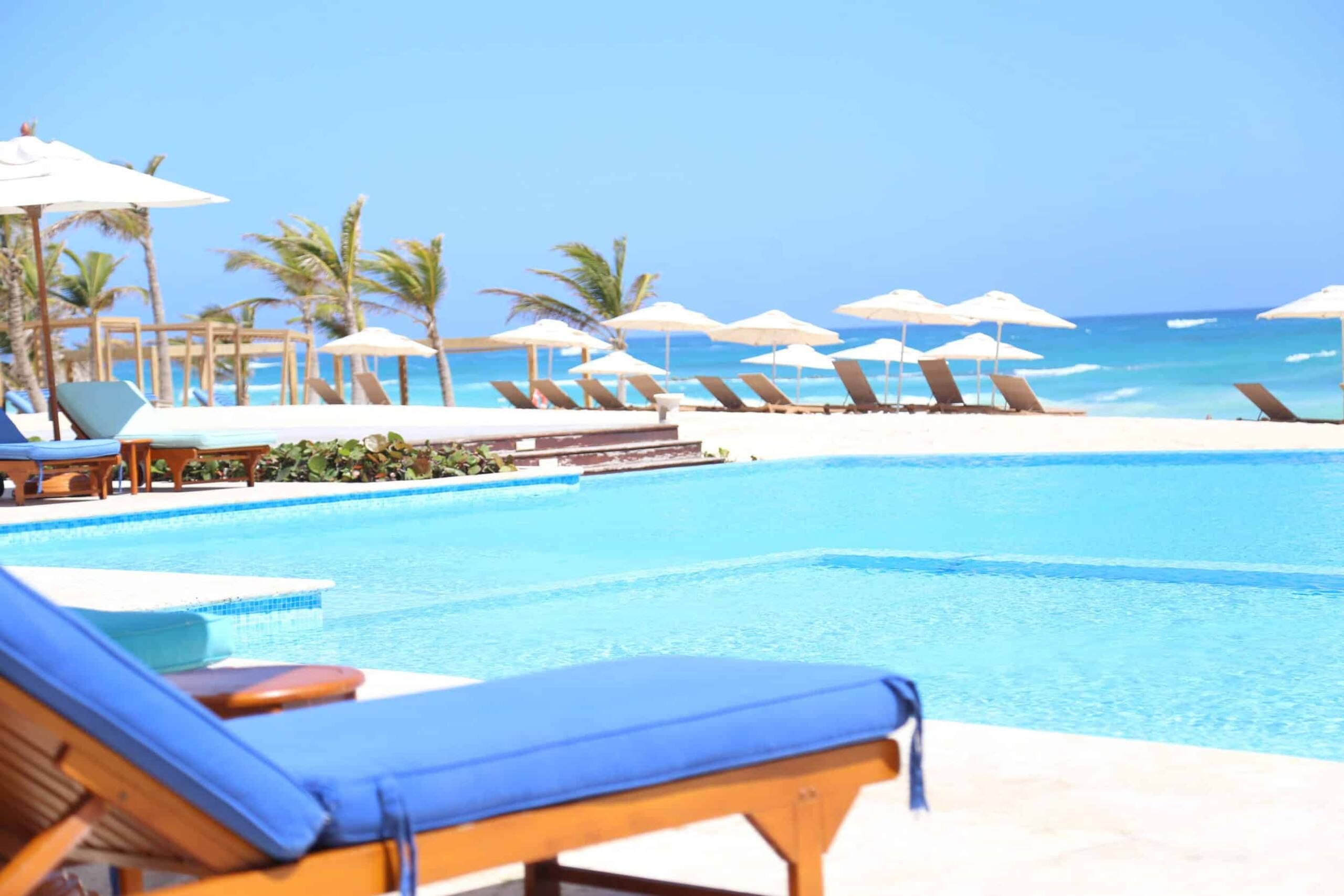 Tumbona azul junto a la piscina del beach club con el mar Caribe detrás