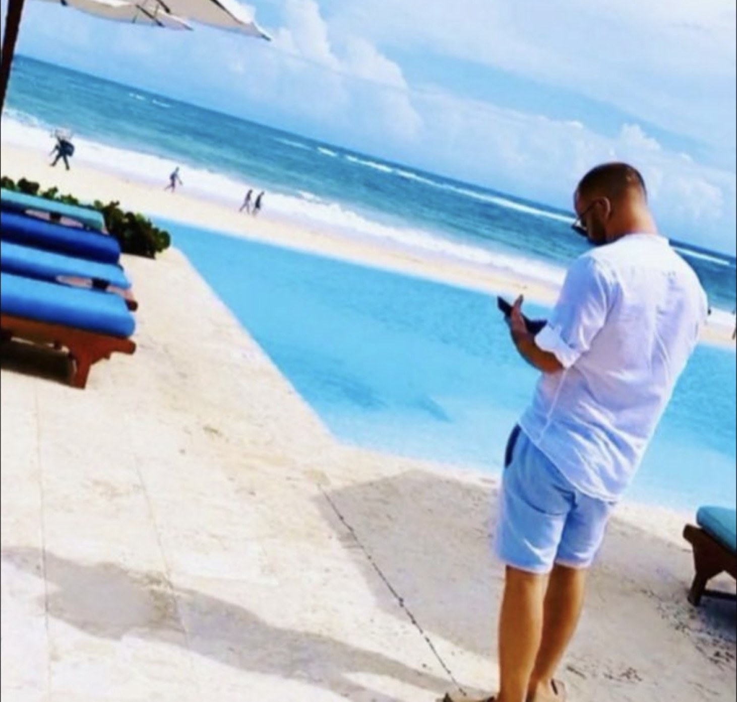 The owner of Swim Up Punta Cana standing by a beach club pool with the sea behind